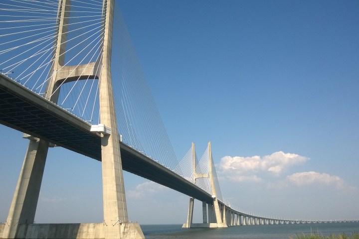 Cable-stayed bridge over water with clear blue sky and clouds.