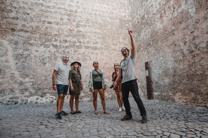 a group of people walking down a sidewalk next to a brick wall