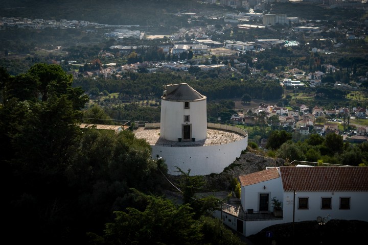 White round building on hill with trees and distant city view.