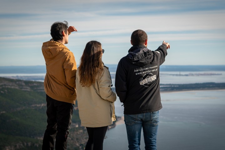 Three people standing on a hill overlooking a scenic coastal view.