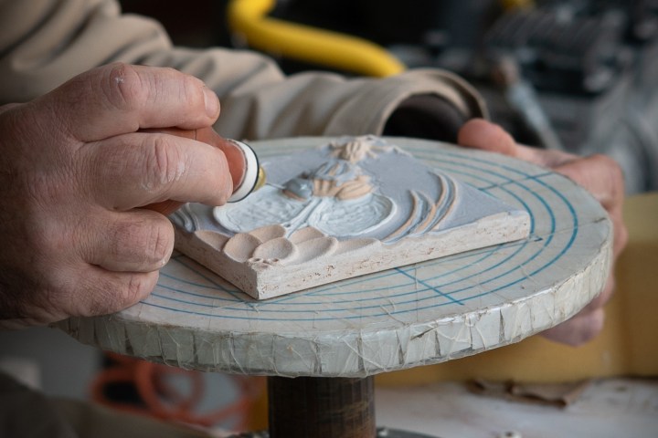 Person carving a design on a rotating stand with a sculpting tool.