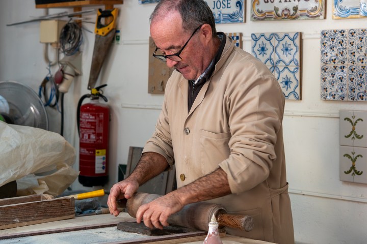 Person shaping clay on a table in a workshop with decorated tiles on the wall.