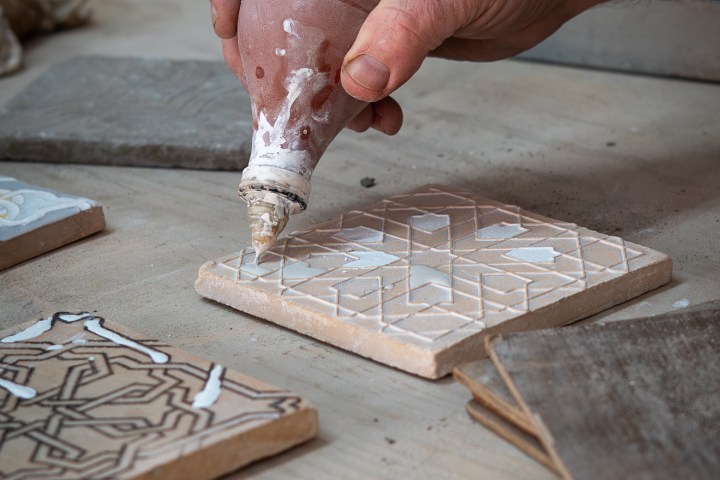 Hand applying white paste on patterned tile with a squeeze bottle.