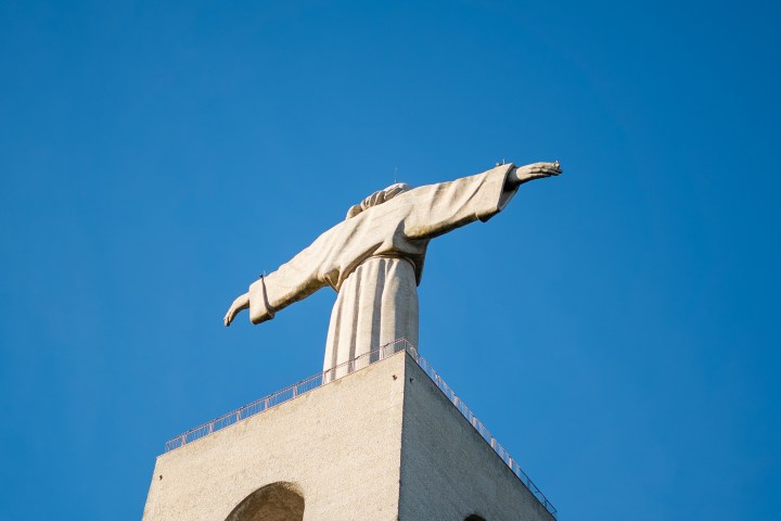Statue of Jesus with outstretched arms against a clear blue sky, viewed from below.