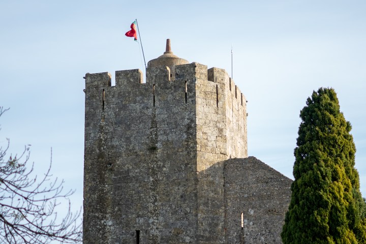 Stone tower with flag flying above, surrounded by tall trees on a clear day.