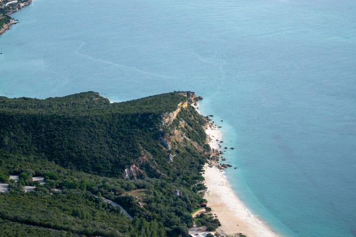 Aerial view of a green peninsula with a sandy beach and clear blue sea.