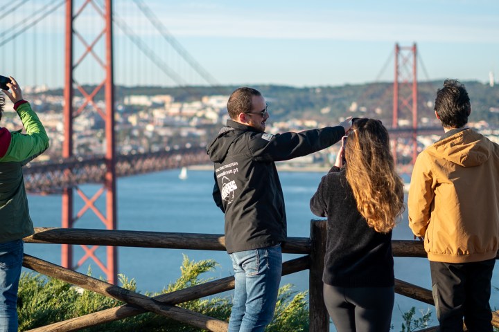 Four people taking photos of a large suspension bridge over a river.