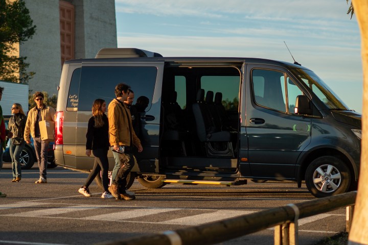 People walking near a gray van with an open door in a parking area.