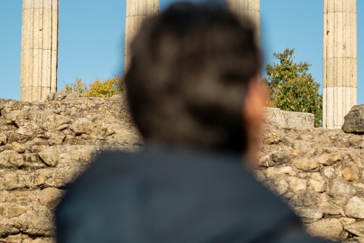 Person with backpack looking at ancient stone columns under a blue sky.