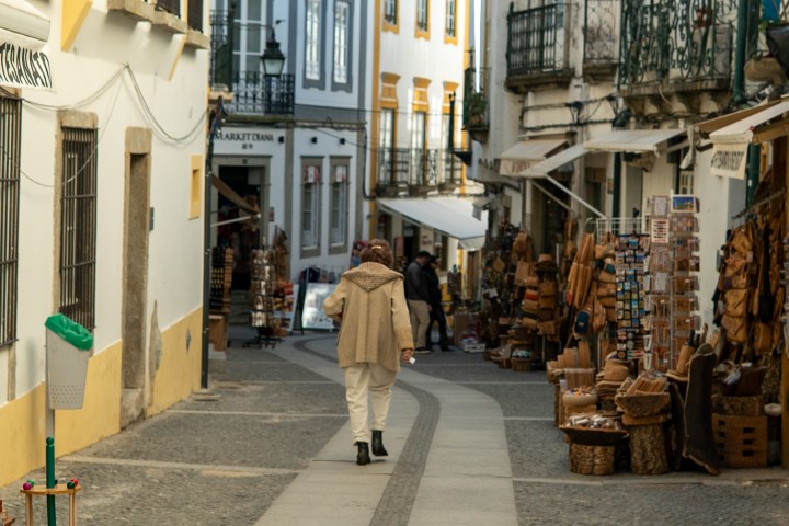 Person walking down a narrow, cobblestone street lined with shops and merchandise displays.