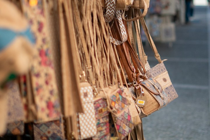 Rack of colorful cork bags displayed on a street market with a cobblestone path.