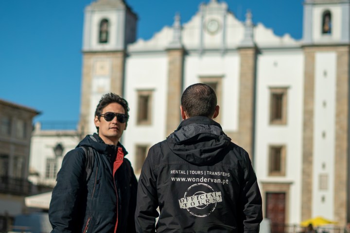 Two people standing in front of a large church building with clear blue sky.