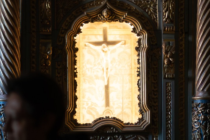 Intricate altar with illuminated crucifix and blurred person in foreground.