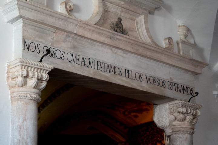 Stone archway with inscription in Portuguese and ornate columns, leading to a dim interior.
