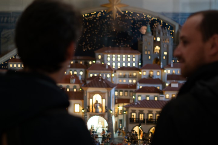 Two people viewing a detailed miniature cityscape with lit buildings.