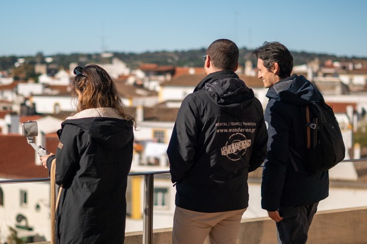 Three people in jackets overlooking a cityscape with rooftops and distant hills.