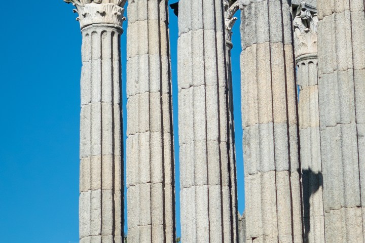 Ancient stone columns with ornate capitals against a clear blue sky.