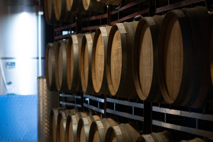 Stacked wooden barrels in a dimly lit winery storage area.