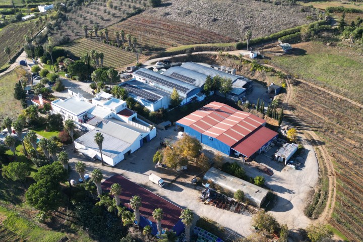 Aerial view of farm buildings and fields, with hills and a distant town.