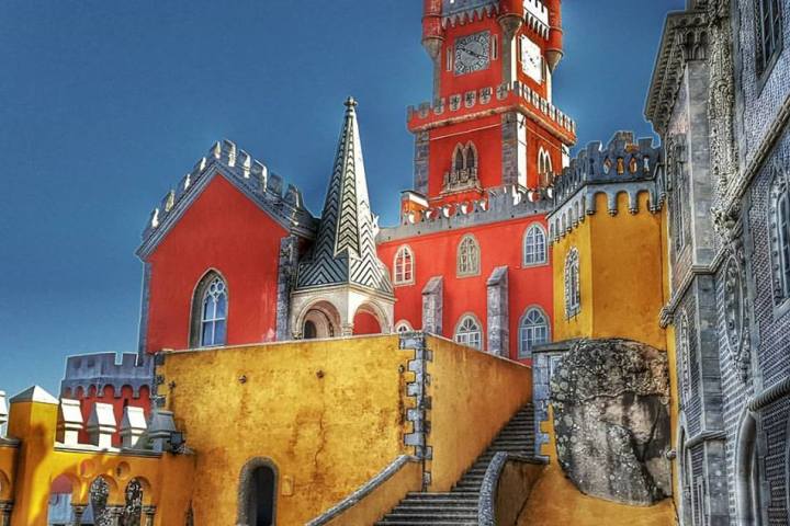 Vibrant yellow and red palace with clock tower and staircase under a clear blue sky.