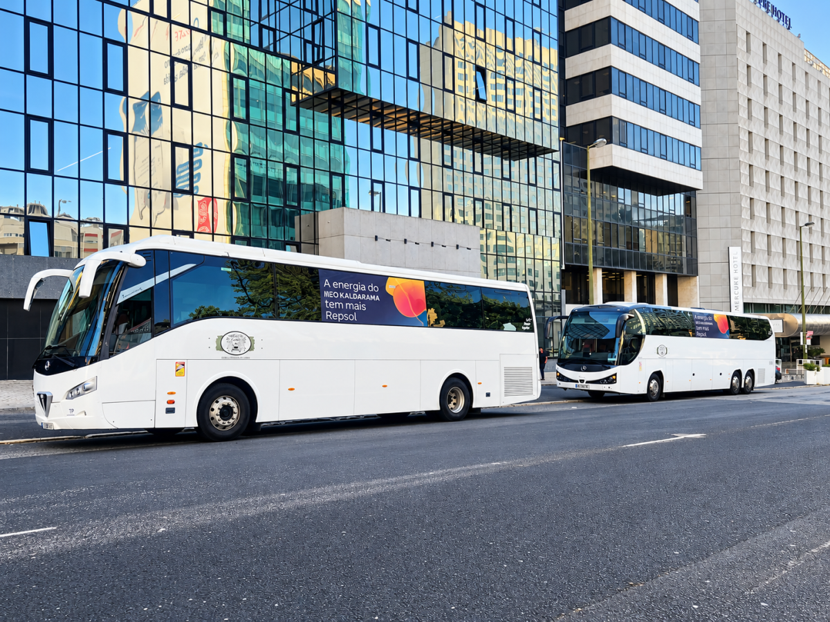 Two white buses parked on a city street near modern buildings.