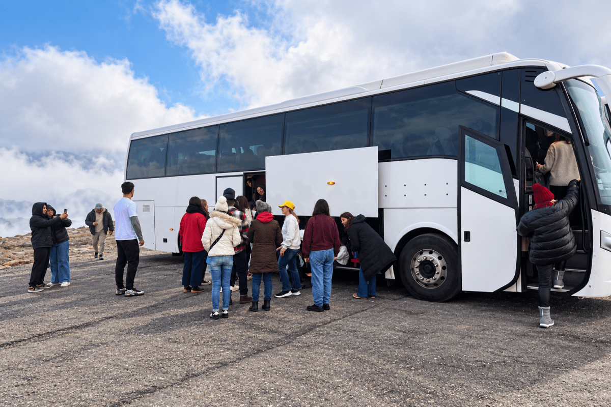 Group of people boarding a white tour bus on a cloudy day.